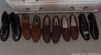 All five pairs of men's shoes arranged side by side on grey carpet, showing variety in color and styles.