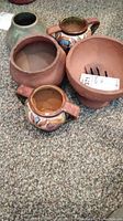 Five pottery pieces arranged on carpet floor: three unglazed terracotta vessels and two colorful hand-painted ceramic vessels with handles.