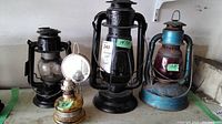 Full view of all four lamps including three railroad lanterns and one glass oil lamp with reflective backplate.
