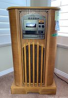 Front view of gramophone style stereo with wooden cabinet, cassette deck, radio tuner, and slatted speaker grill.