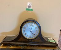 Full side view of wooden mantel clock with classic curved shape and decorative inlays on the base.