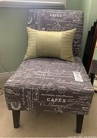 View of side chair showing dark upholstery with white script text and a beige decorative throw pillow placed on the seat