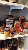 Shelf with various vintage spice tins including Rauteigh's Mustard, Keen's Mustard, Young Lime, Club House Poultry Dressing, Schwartz Cream of Tartar, and others.