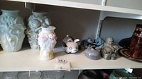 Light blue floral ceramic vases, Delft hand-painted piggy bank pig figurine, and two bear figurines with ear chips on white shelving.