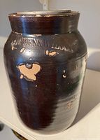 Side view showing one dark glazed pottery jar with embossed marking "Cowden & Wilcox" and multiple areas of glaze chipping.