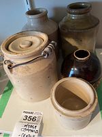 Five vintage pottery pieces including one jar with wire handle and lid, showing surface crazing and age wear.