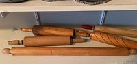 Five wooden rolling pins arranged on a shelf showing varying lengths and handle styles