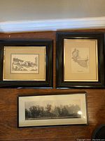 Three framed black and white prints arranged on floor: two signed landscape drawings by Nevin Robinson of Pittsburgh landmarks, one panoramic city street photograph