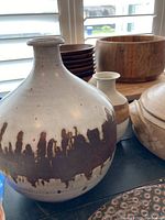 Large rounded stoneware pot with narrow neck featuring dark brown drip glaze over off-white speckled ceramic, signed on bottom.