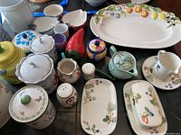 Full view of the ceramic service ware collection showing platter, canisters, salt shaker, creamer, butter dish, jelly dishes, candle holders and small cups.