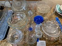 Overview of assorted glass dishes on countertop including clear cut glass bowls, milk glass items and a blue glass bowl.