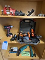 Shelf display of drills, chargers, battery tester, and chainsaw parts with carrying case and level