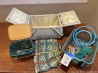 Photo showing large open woven sewing basket with cream-colored fabric lining along with other baskets and crafting supplies on wooden surface.