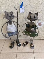 Front view showing both metal cat sculptures side by side against a wall.