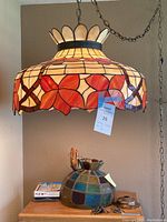 Large stained glass hanging lamp turned on showing red flower motifs and cream yellow glass with dark metal framing, hanging by a chain from ceiling.