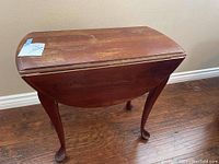 Closed view of the vintage fold down side table showing the rectangular top with visible wear and scratches, cabriole legs ending in pad feet, and folded side panels.