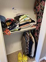 Closet scene with assorted women's clothing folded on shelf and hung below, including jackets and kilts. Yellow Tweety Bird slippers on floor.