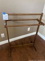 Wooden quilt and blanket holder standing against a beige wall with two horizontal bars.