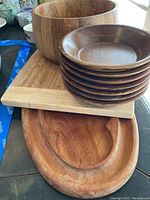 Large wood salad bowl, stacked smaller wooden side bowls, bamboo cutting board and wooden charcuterie board arranged on tabletop