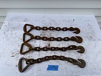 Four chain extenders laid flat on a white surface showing triangular rings and hooks, visible rust and wear.