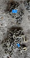 Pair of coiled steel chains with attached clevis hooks on a concrete floor.