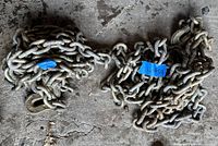 Pair of heavy-duty metal chains with clevis hooks laid on concrete floor, showing total length and condition.