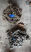 Two 3/8 inch thick chains coiled on the ground with blue tape marks.