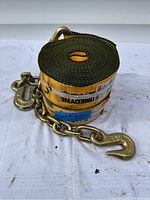 Pair of rolled yellow 3 inch winch straps with attached gold-colored metal chains and hooks lying on a white surface.