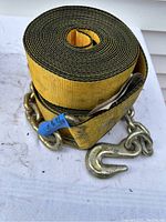 Rolled yellow winch strap showing metal chain anchor hooks attached.