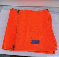Stack of six folded fluorescent orange mesh load flags with black edge stitching and visible corner metal grommets.