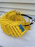 Eighteen yellow plastic corner guards arranged side by side and held with a black strap, showing their shape and cutouts