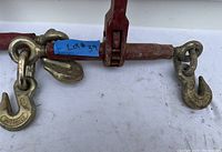 Close-up of one ratchet load binder showing hook ends with embossed markings and blue tape label.