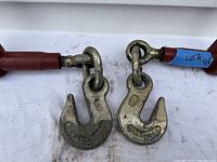 Close-up photo showing the large metal hooks connected to chain links of the ratchet load binders, demonstrating their robust and heavy-duty construction.