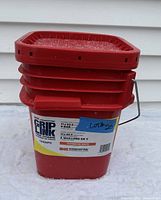 Red pail labeled 'Grip Link' containing tire chains, front view with visible product information including size 11x22.5 and Kinedyne brand.