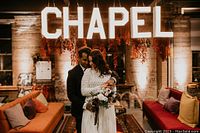 Couple standing in front of illuminated ‘CHAPEL’ sign in a decorated venue