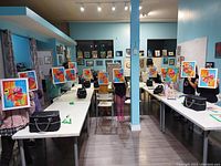 Children seated at long tables in studio holding up colorful flower paintings