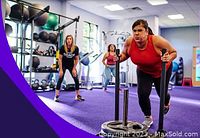 Group fitness session with participant pushing weight sled in gym setting