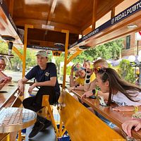 Group of riders and guide aboard wooden Pedal Pub bike with overhead canopy, branded PedalPubToronto signage