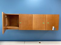 Front view of the wooden four-door wall cabinet with the leftmost door open showing interior shelf