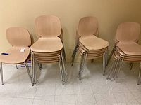 Stacked light wooden chairs with chrome metal legs against a beige wall on tiled floor.