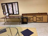 Three long folding tables stacked with one set up, and black metal folding cart beside them.