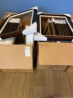 Two large boxes filled with stacked burl style picture frames, showing golden and silver finishes with corner protectors and foam padding.