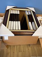 Top view of the box showing several burl wood picture frames with gold and silver trim stacked neatly with corner protectors.