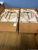 Two boxes containing white wash picture frames with gold and silver trim set inside with foam padding and cardboard corner protectors.