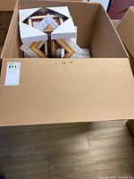 Top view of large cardboard box full of individually boxed picture frames with white protective corner cardboard pieces.