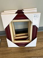 Two stacked wooden picture frames with protective corner covers. Larger frame is reddish-brown, smaller frame inside is light wood with gold trim.