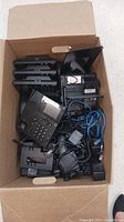 A cardboard box filled with multiple black office IP phones and various cables and equipment.