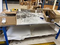 Metal shelf with picture frame hanging wires, boxes containing hardware and accessories on a white cloth covering