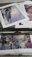 Grey three-drawer cabinet top with loose canvas prints showing a winter waterfall scene and a snowy village street.