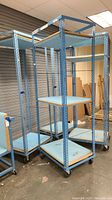 Photo showing three light blue metal storage racks with shelves and caster wheels